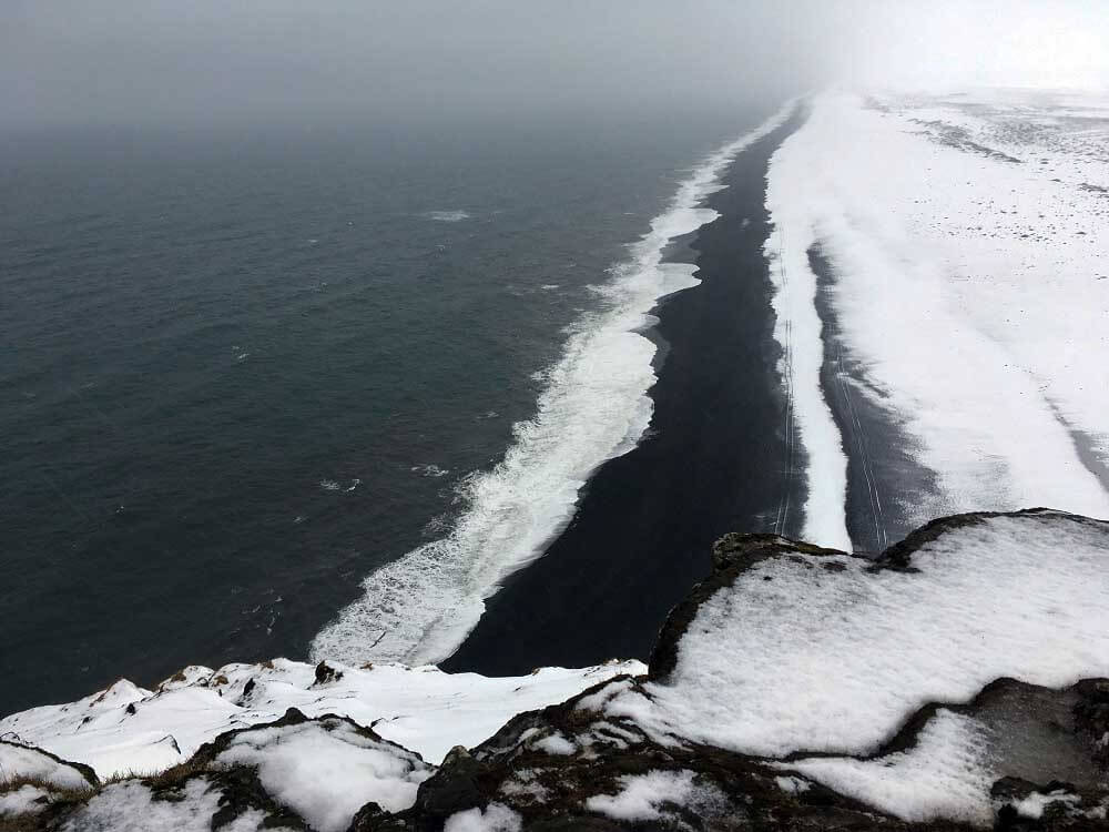 Der schwarze Strand bei Vik vom Kap Dyrholaey aus wirkt im Winter mit Schnee fast unwirklich.