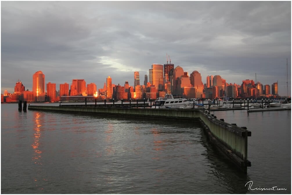 Die Skyline wird von der untergehende Sonne in einem unwirklichen orange angestrahlt. Diesen BLick genießt man vom Jersey Boardwalk in der Nähe des Holland Tunnels